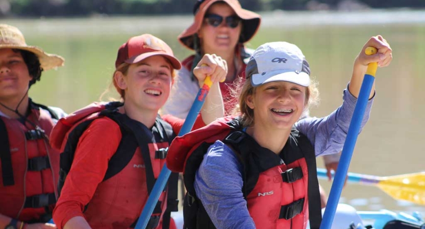 Young people wearing lifejackets hold the oars of a raft